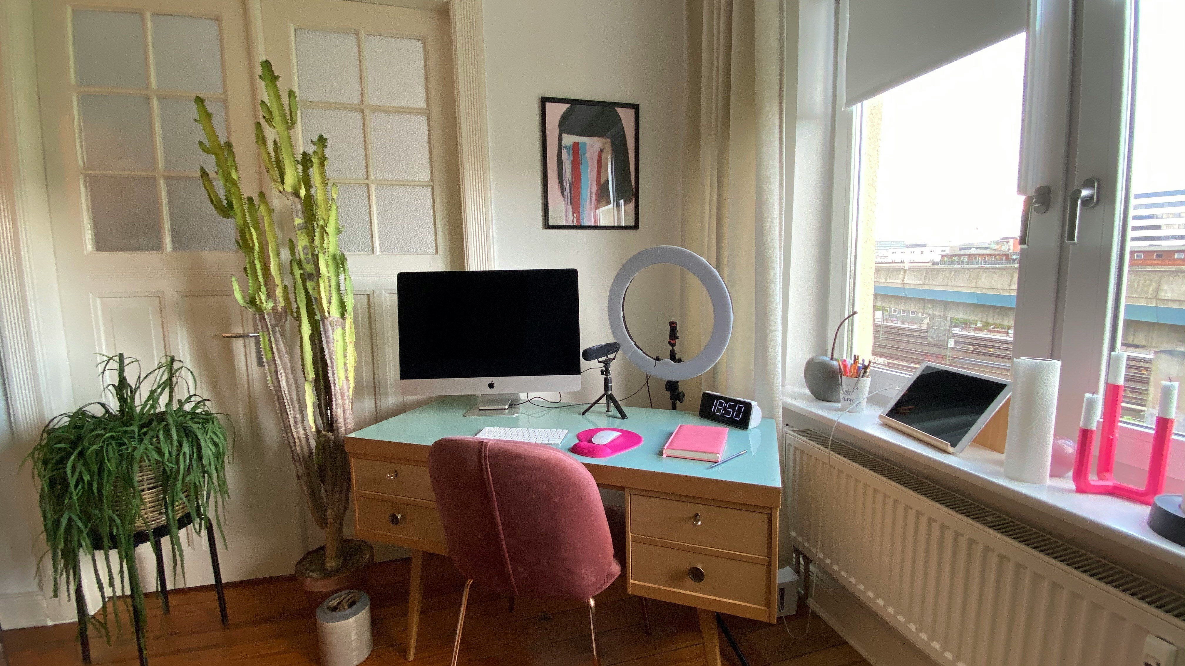 At home office desk in the corner with ring light, mac computer, windows and plants