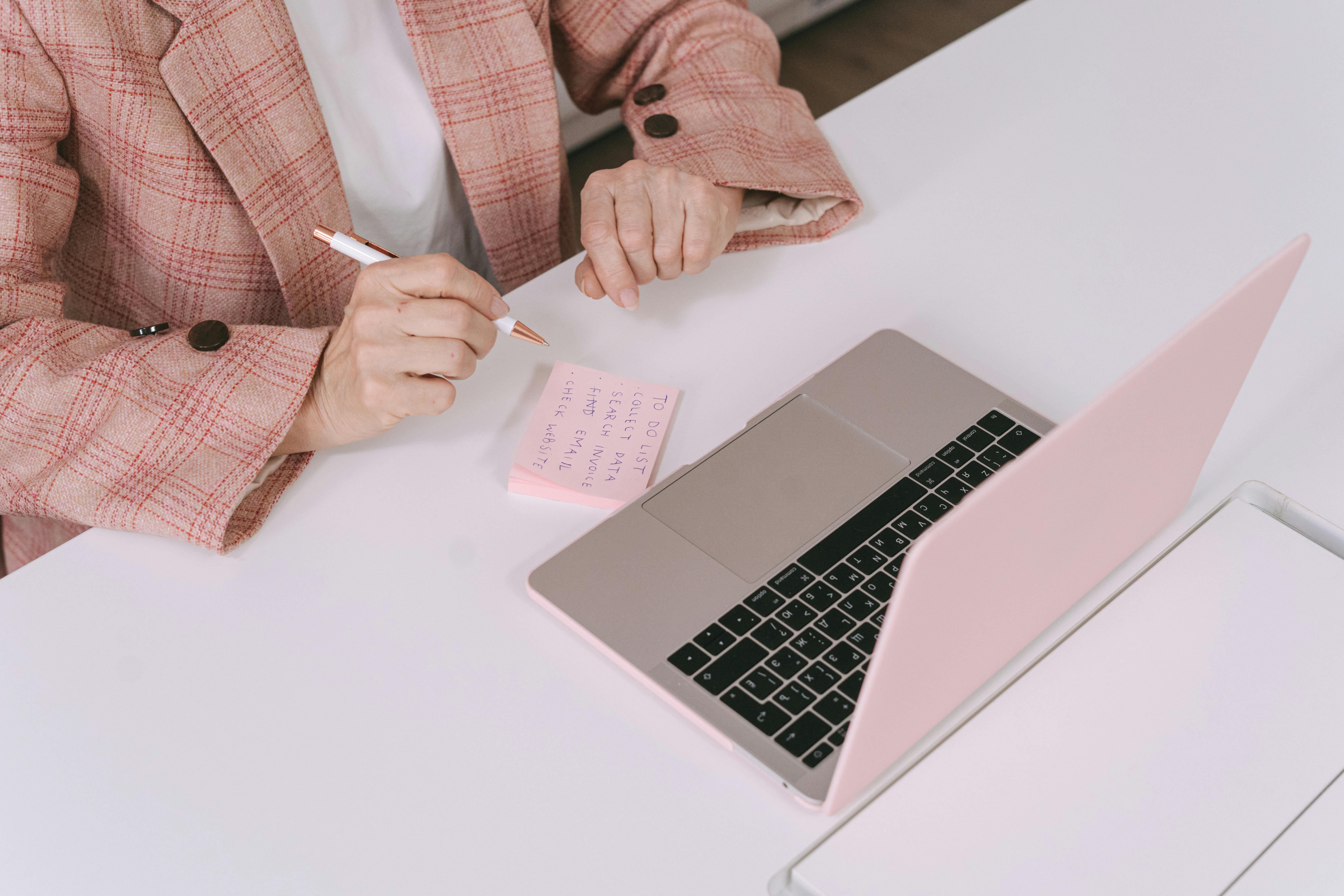 pink mac book with female writing on pink sticky note with pink plaid blazer